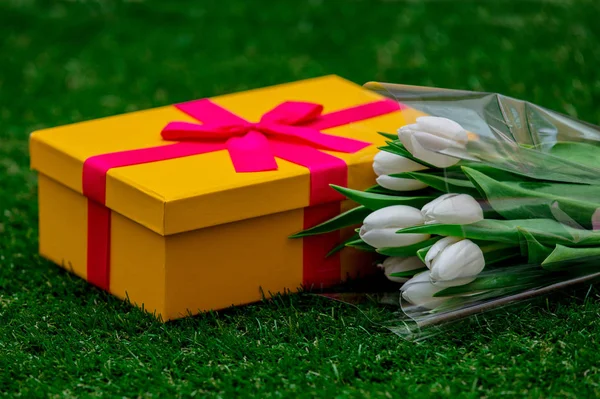 Dárková krabice s růžovou mašličkou a tulipány na zelené trávě trávníku — Stock fotografie