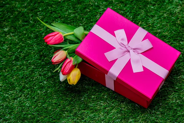 Caja de regalo y tulipanes en césped de hierba verde —  Fotos de Stock