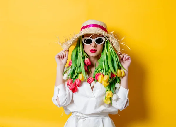 Vrouw in wit shirt en muts met verse lente tulpen en zonnebril — Stockfoto
