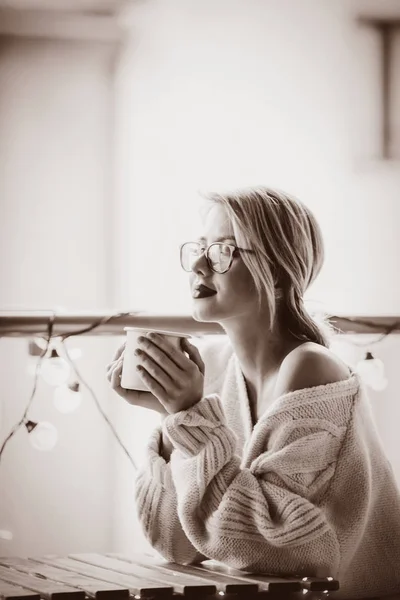 Jonge vrouw met kopje koffie in de buurt van fairy lichten — Stockfoto