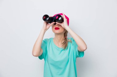 Güzel genç kız pembe kap ve mavi t-shirt beyaz arka plan üzerinde dürbün ile bir şey arıyor.