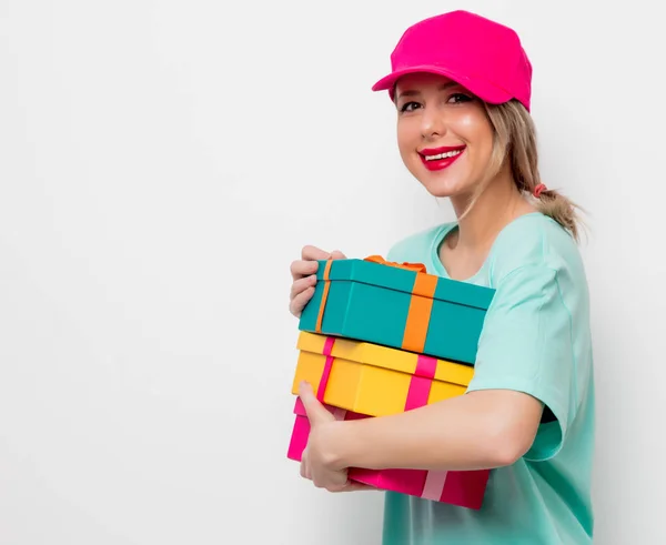 美丽的年轻女孩在粉红色的帽子和蓝色的 T恤与假日礼物箱子在白色背景 — 图库照片