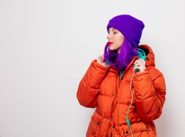 Güzel genç kız mor saçlı ve turuncu ceketli beyaz arka plan üzerinde kulaklık müzik dinle.