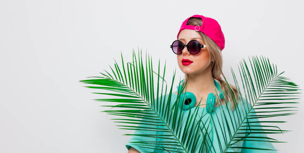 Beautiful young girl in pink cap and blue t-shirt with green palm branch on white background.