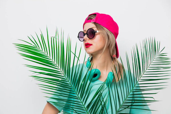 Beautiful young girl in pink cap and blue t-shirt with green palm branch on white background.