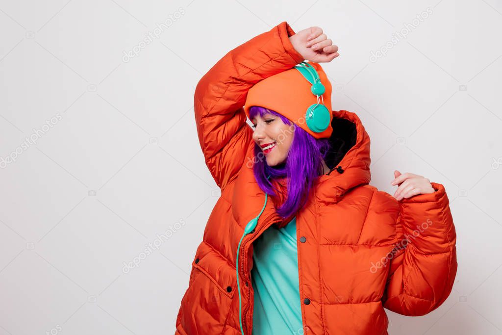 Beautiful young girl with purple hair and in orange jacket listen music in headphones on white background.