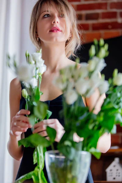 Fille dans une robe noire tient des roses blanches avant de les mettre dans un vase — Photo