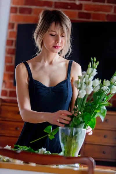 Flicka i en svart klänning håller vita rosor innan du lägger dem i en vas — Stockfoto