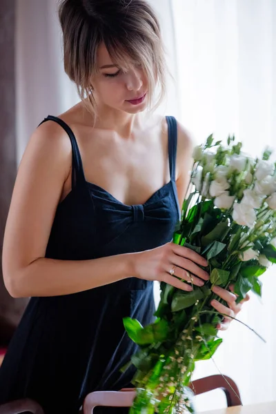 Dziewczyna w czarnej sukni trzyma białe róże przed wprowadzeniem ich w wazonie — Zdjęcie stockowe