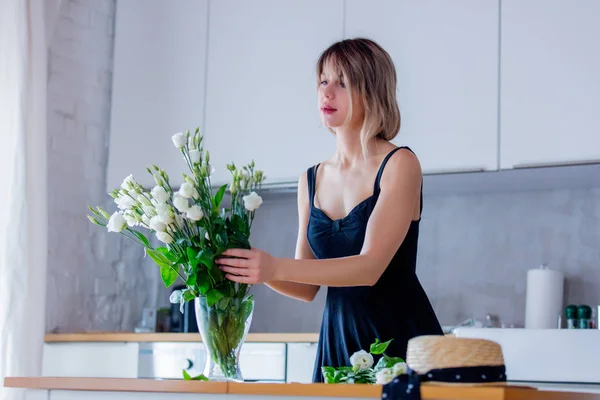 Chica en un vestido negro está sosteniendo rosas blancas antes de ponerlos en un jarrón —  Fotos de Stock