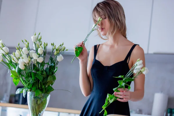 Fille dans une robe noire tient des roses blanches avant de les mettre dans un vase — Photo