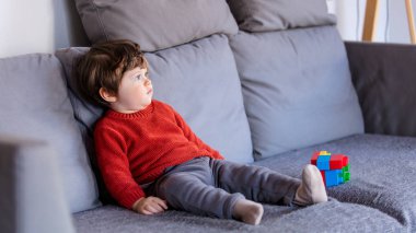 Komik küçük çocuk kırmızı kazaklı kanepede oturuyor. Yan görünüm 