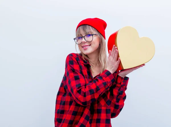 Woman in red shirt and hat holding heart shape gift box — Stock Photo, Image