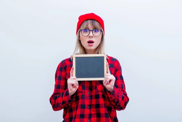 Jonge vrouw in een rood shirt en muts met schoolbord — Stockfoto