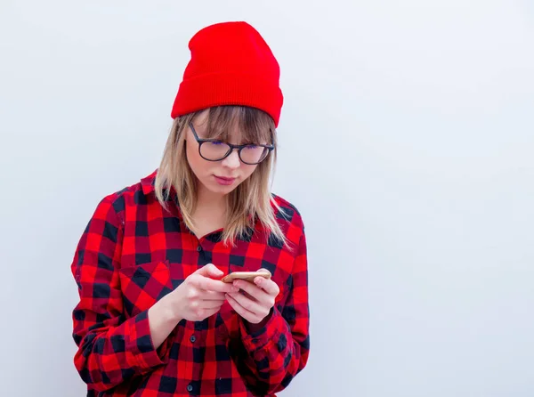 Jonge vrouw in een rood shirt en muts met mobiele telefoon — Stockfoto