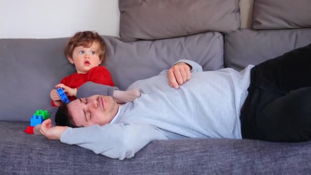 Chłopiec siedzi na kanapie w pobliżu zmęczony ojca we śnie — Wideo stockowe