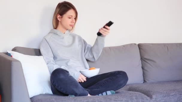 Young woman is holding remote control and watching TV — Stock Video