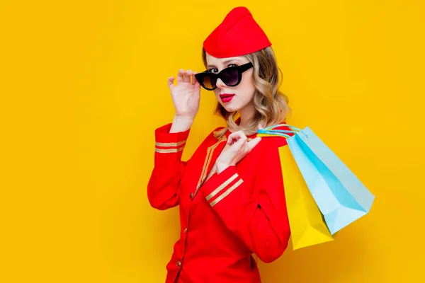 穿着红色制服 穿着购物袋的迷人的复古空姐的肖像 在黄色背景上隔离 — 图库照片