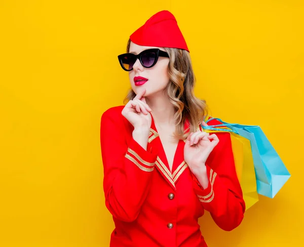 赤いショッピング バッグと制服を着て魅力的なヴィンテージ スチュワーデスの肖像画 黄色の背景に分離 — ストック写真