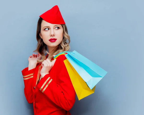 赤いショッピング バッグと制服を着て魅力的なヴィンテージ スチュワーデスの肖像画 灰色の背景に分離 — ストック写真