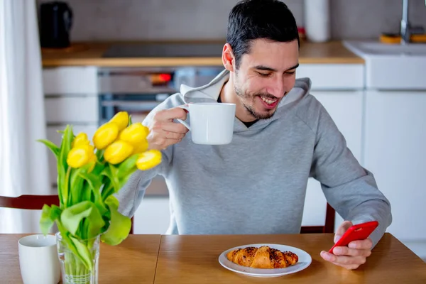 Hombre sentado en la mesa con taza de café o té y teléfono móvil —  Fotos de Stock