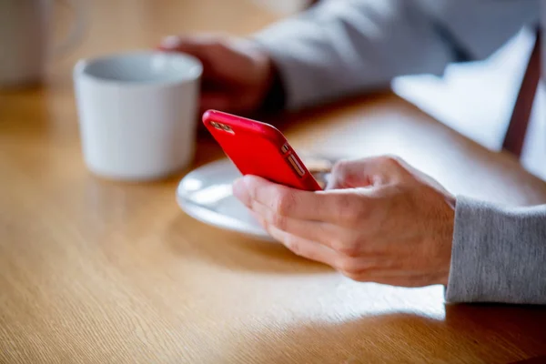 Hombre sentado en la mesa con taza de café o té y teléfono móvil . — Foto de Stock