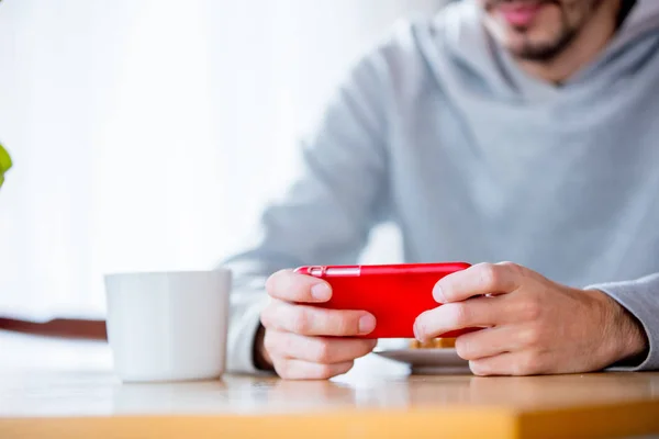 Homem sentado à mesa com xícara de café ou chá e telefone celular . — Fotografia de Stock