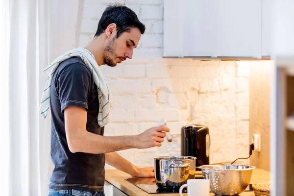 Junger Mann in schwarzem Hemd kocht zu Hause in Küche. — Stockfoto