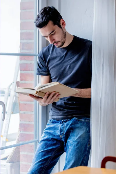 Young man with book staying near window