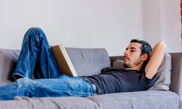 Echter Mann legt sich auf Sofa und liest ein Buch. — Stockfoto