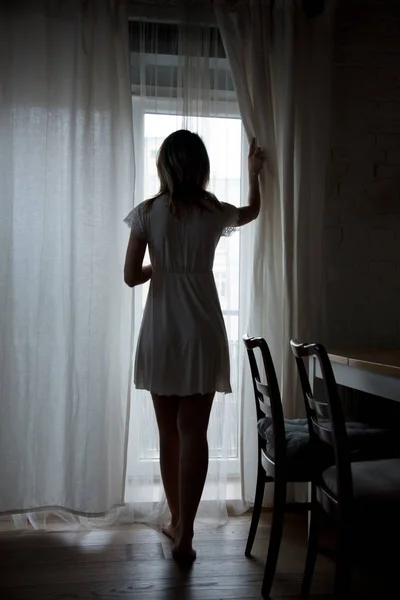 A young girl looks behind the curtains — Stock Photo, Image