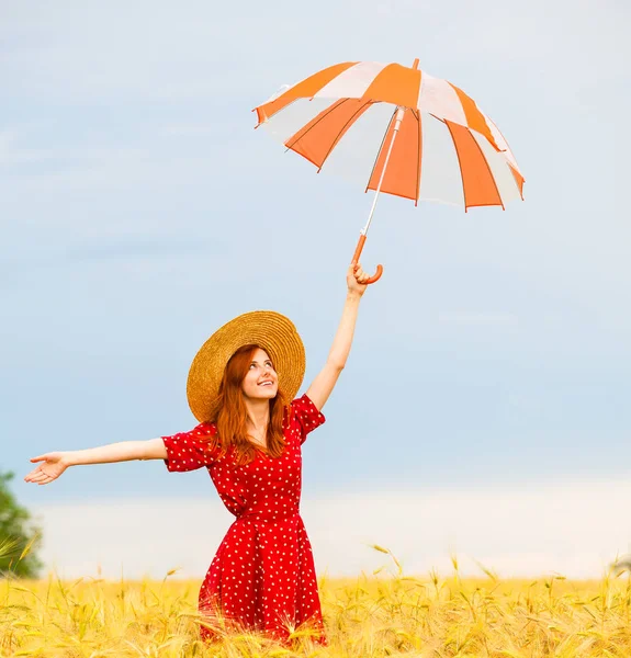 Руда дівчина з парасолькою на пшеничному полі — стокове фото