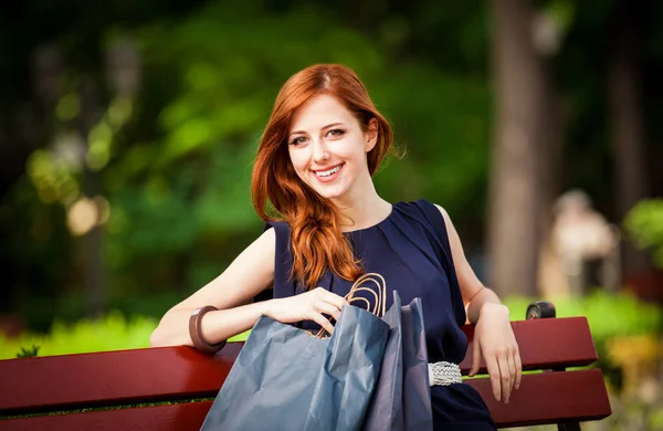 赤毛の買い物袋でベンチに座っている女性のスタイルします。 — ストック写真