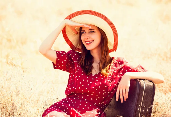 Рыжая девушка с чемоданом сидит на траве — стоковое фото