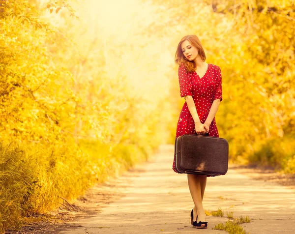 Κοκκινομάλλα κορίτσι με τη βαλίτσα στο σοκάκι του δέντρου. — Φωτογραφία Αρχείου