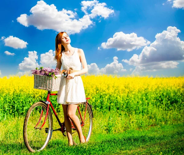 Rödhårig tjej med cykel och blommor i korg — Stockfoto