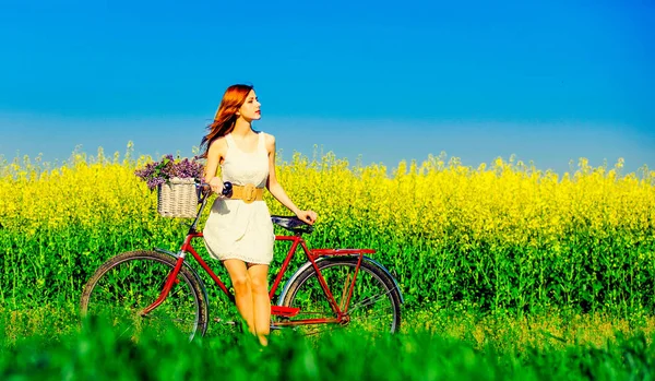 Рыжая девушка с велосипедом и цветами в корзине — стоковое фото