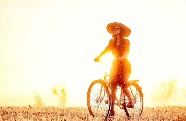 Menina de bicicleta no campo na hora do nascer do sol — Fotografia de Stock