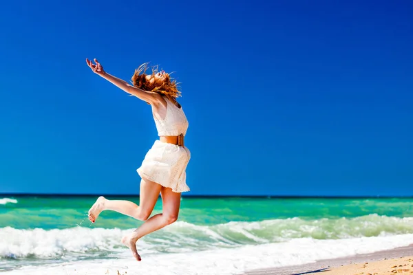 Unga rödhårig flicka hoppande på stranden. — Stockfoto