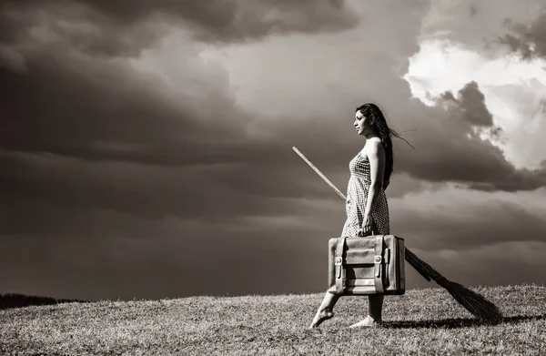 Young witch at grass field with broom in storm day. — Stock Photo, Image