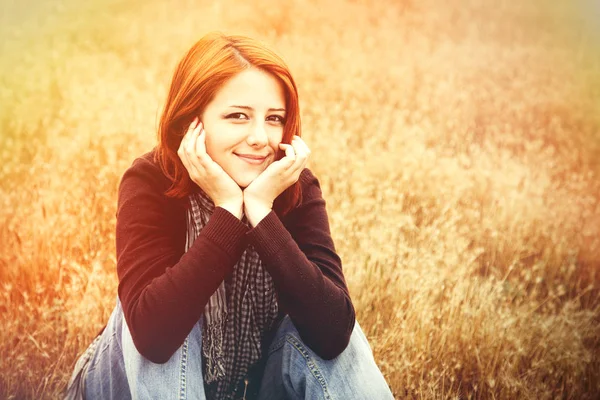 Mooi roodharig meisje zitten op gele herfst gras. — Stockfoto