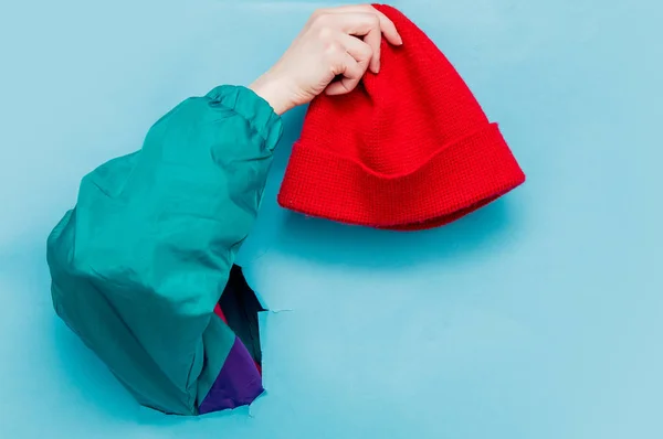 Female hand in 90s style jacket holding red hat — Stock Photo, Image