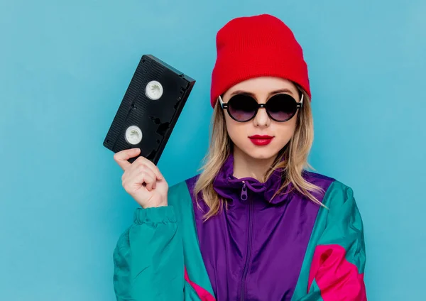 Жінка в червоній шапці, сонцезахисні окуляри та костюм 90-х років з касетою VHS — стокове фото