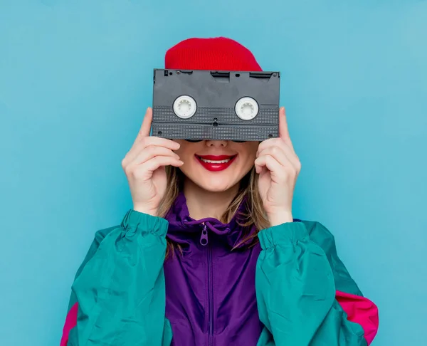 Wanita bertopi merah, kacamata hitam dan setelan 90-an dengan kaset VHS — Stok Foto