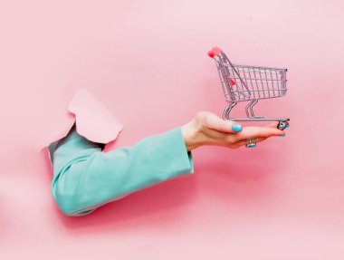 Pembe arka plan alışveriş sepeti ile klasik mavi ceketli el bakıyor