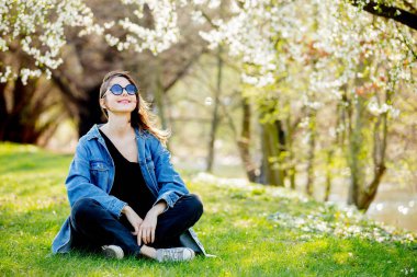 Bir denim ceket ve güneş gözlüğü bir flowe yakın oturan genç kız
