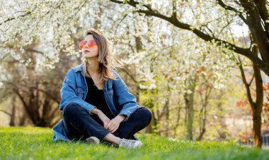 Bir denim ceket ve güneş gözlüğü bir flowe yakın oturan genç kız