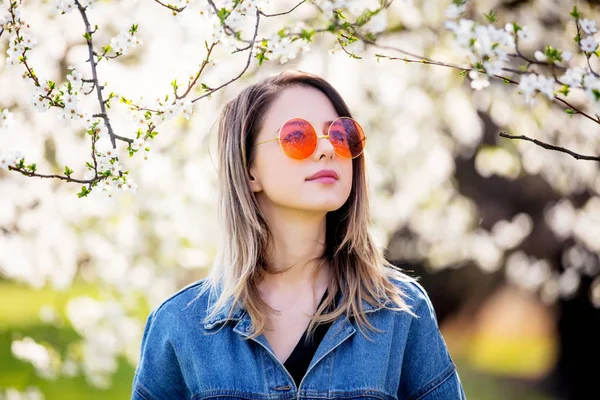 Mladá dívka v džínovou bundě a sluneční brýle stojí nedaleko květu — Stock fotografie