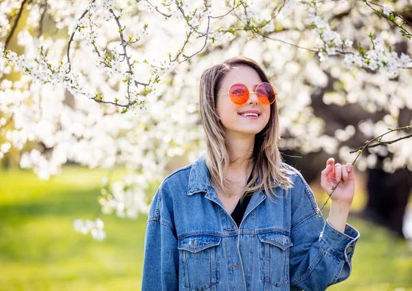 Bir kot ceket ve güneş gözlüğü genç kız bir çiçek yakınında duruyor — Stok fotoğraf