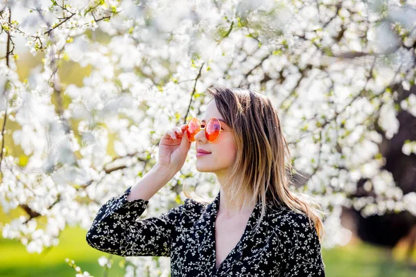 Mladá dívka v slunečních brýlích u kvetoucího stromu — Stock fotografie